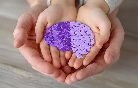 Erwachsene und Kinderhände halten ein Gehirn mit einem Puzzle-Papierausschnitt